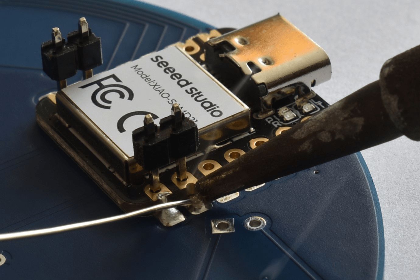 Ein Anschluss des Mikrocontrollers ist verlötet, der zweite wird gerade gelötet. Dabei werden Lötkolben und Lötzinn seitlich an den Mikrocontroller herangeführt.